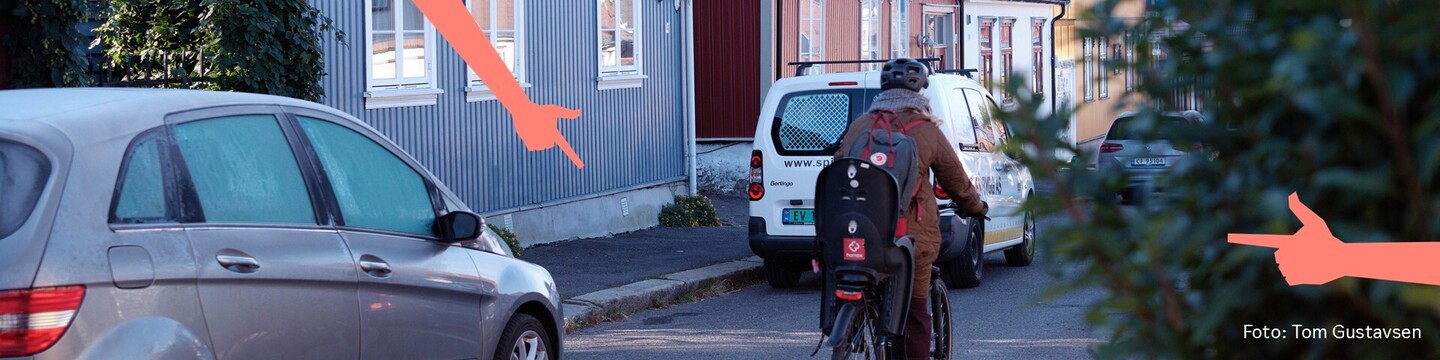Bilde som viser gate med trehus, parkerte biler, syklist