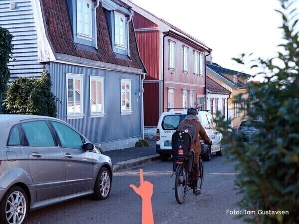 Bilde som viser gate med trehus, parkerte biler, syklist