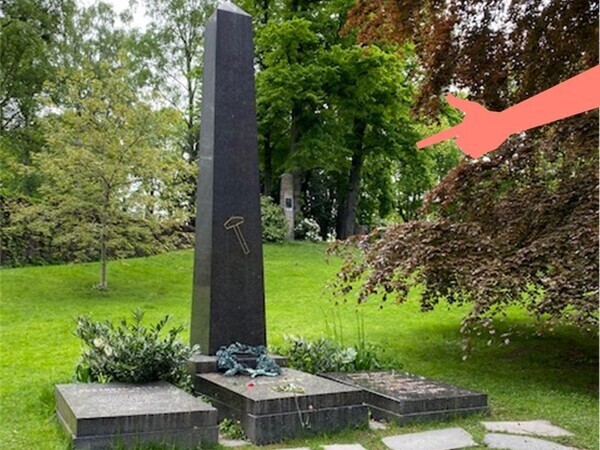Bilde av Henrik Ibsen sin gravplass, med en illustrasjon av pekende hånd som peker mot gravstøtten.